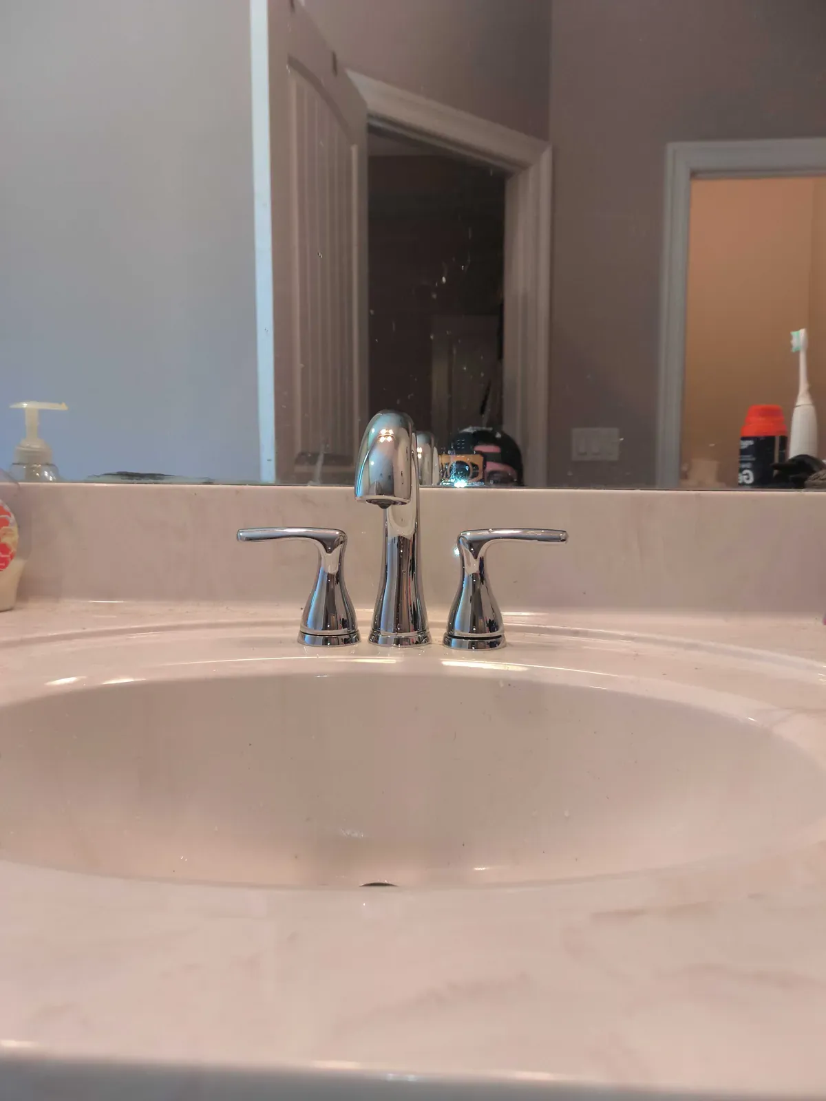 Chrome widespread bathroom faucet with curved spout and lever handles on a light stone countertop with a white undermount sink