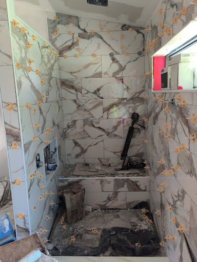 Walk-in shower with large-format marble-pattern tile being installed with orange tile leveling clips during a Florida bathroom renovation