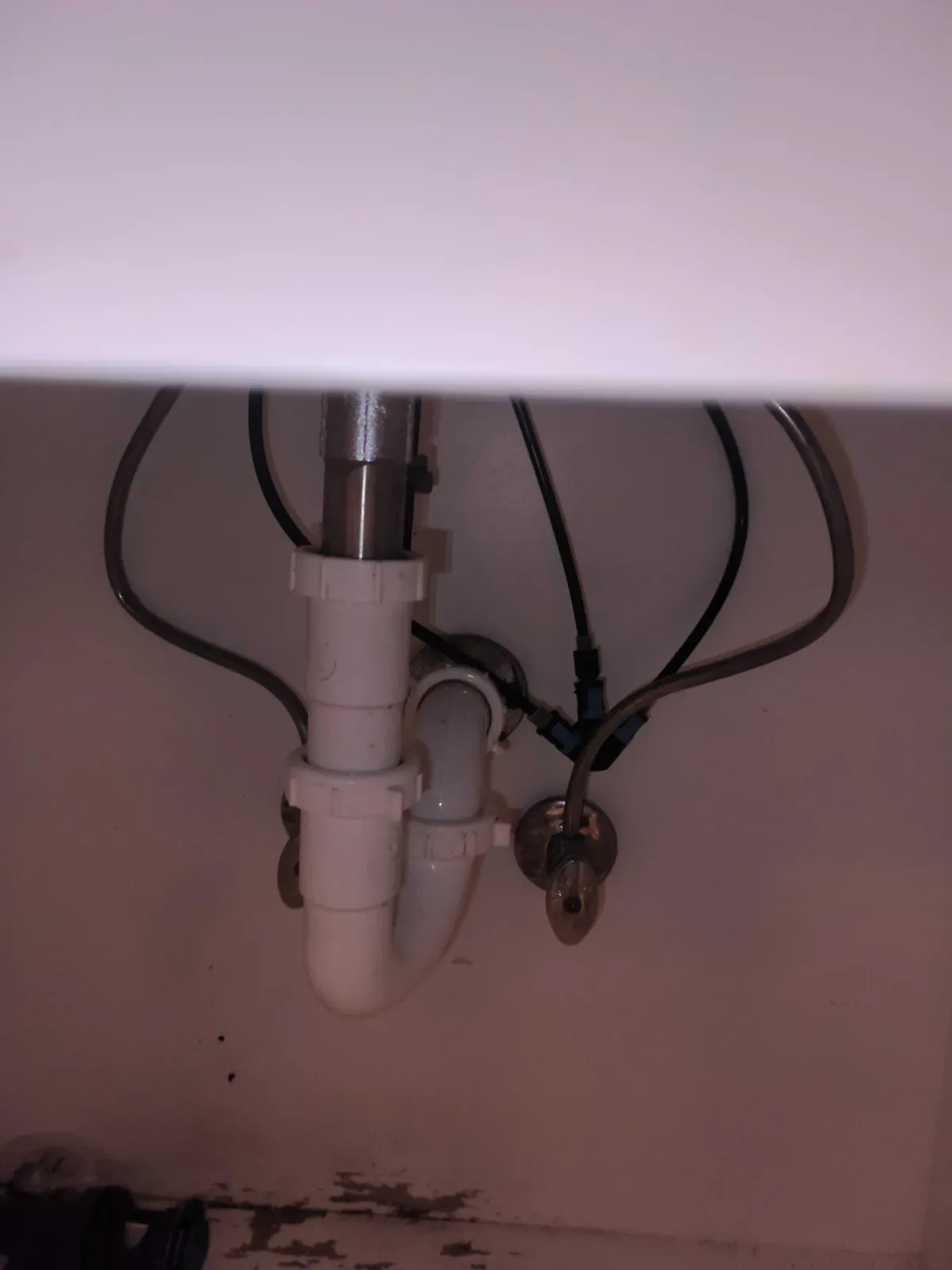 Bathroom vanity plumbing with white PVC P-trap, chrome shutoff valves, and braided water supply lines under a sink