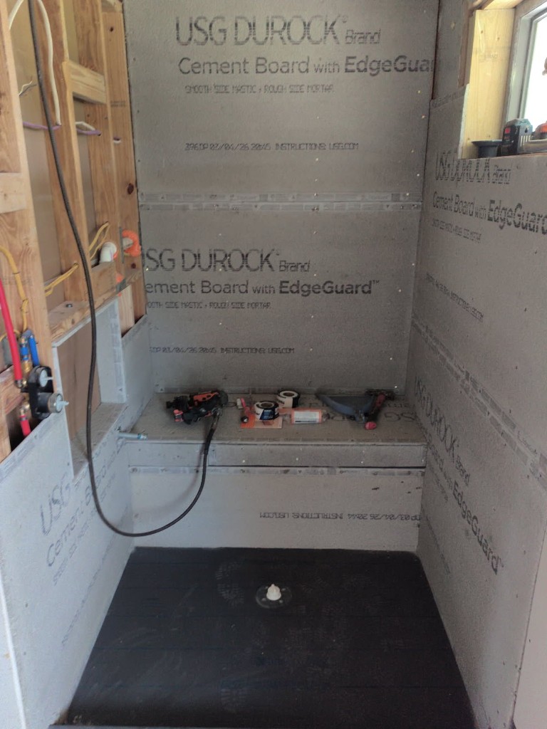 Walk-in shower cement board installation with built-in bench, mesh tape on seams, tools on bench, and waterproof pan liner on floor
