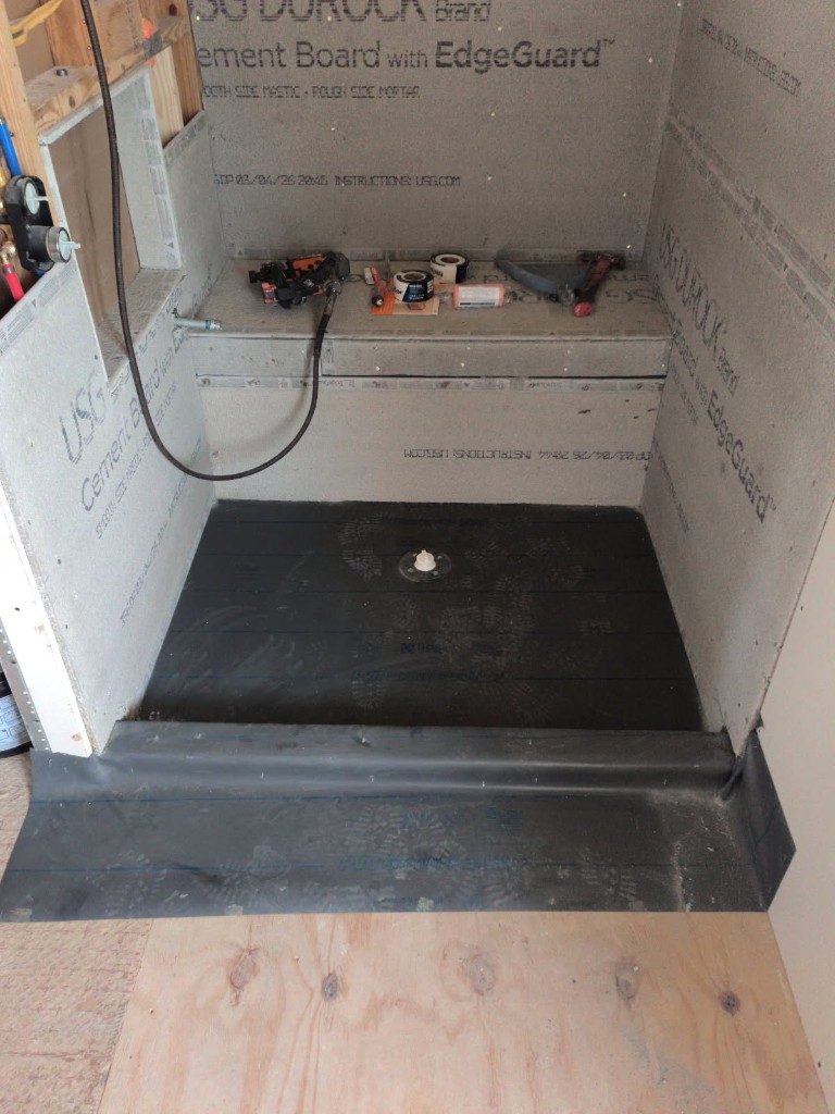 Custom walk-in shower with grey USG Durock cement board walls, built-in bench, black waterproof pan liner, and central drain