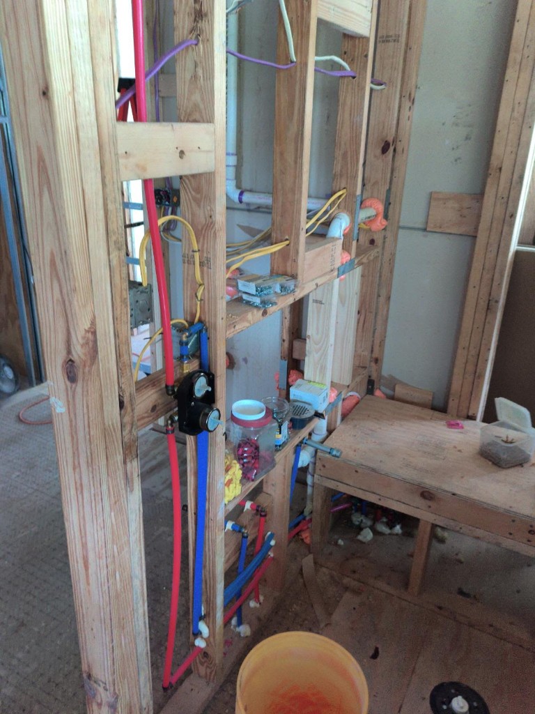 Shower framing rough-in with red and blue PEX water lines, mixing valve, PVC drain, and electrical wiring before cement board installation