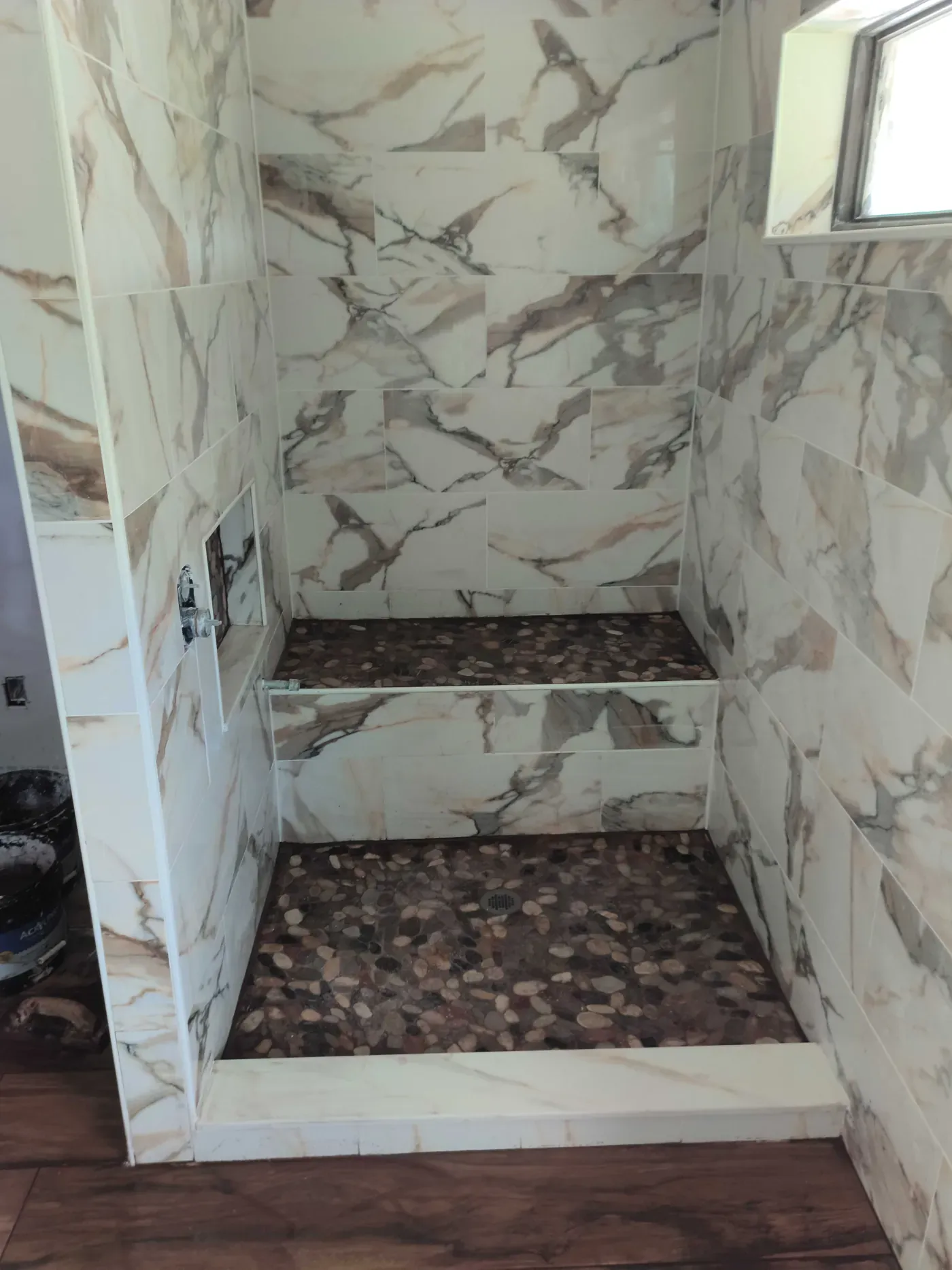 Custom walk-in shower with marble-look wall tile, river rock pebble floor and bench, recessed niche, and chrome valve in a Florida bathroom