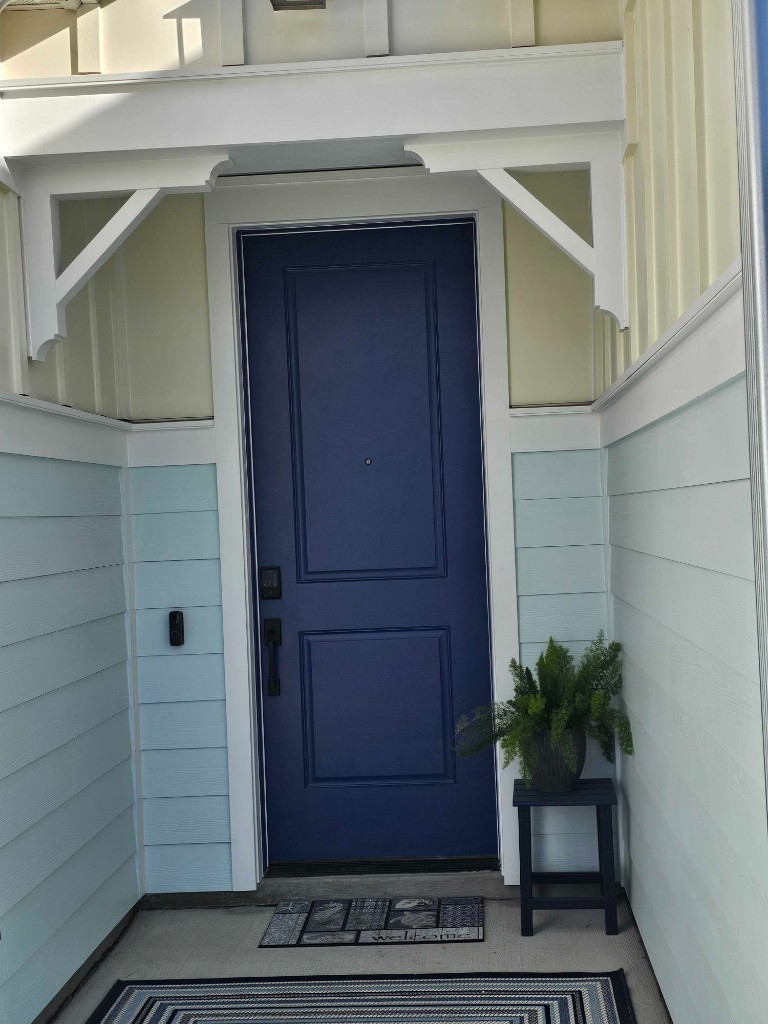 Navy blue front entry door with keypad deadbolt and video doorbell on a coastal-style home
