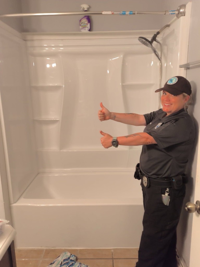 FDC Florida law enforcement officer in uniform giving double thumbs up in front of a newly installed white shower and tub unit