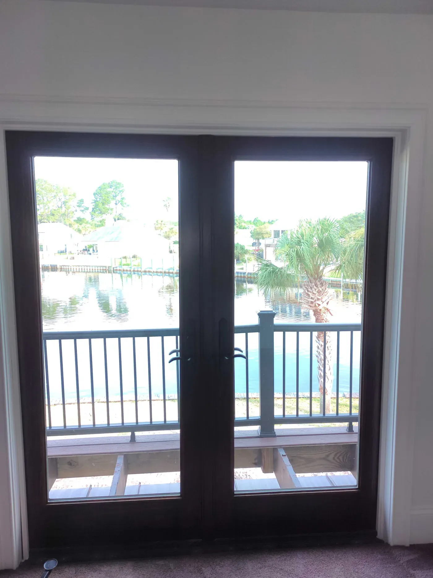Interior view of dark-framed French doors with white trim opening to a wooden deck, canal, and neighboring homes in Florida