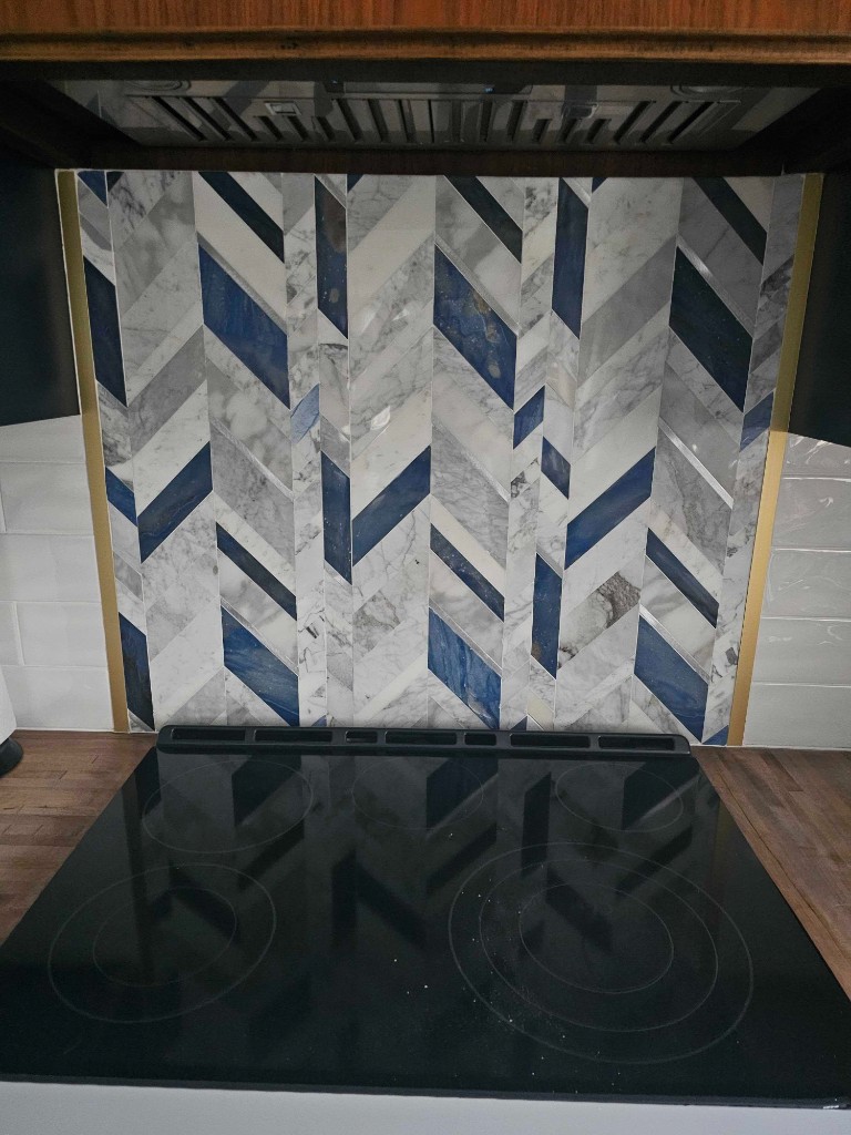 Custom marble and navy tile kitchen backsplash installation behind a glass cooktop