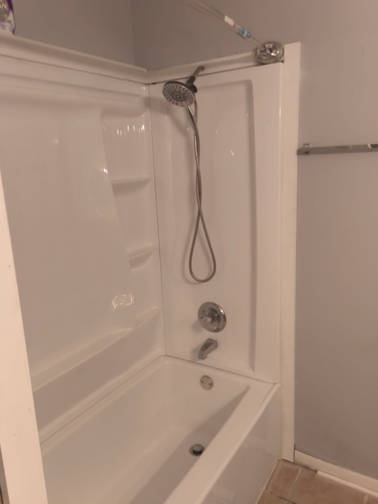 Newly installed white one-piece shower and tub combo with chrome handheld shower head and faucet, side angle view inside a Florida bathroom