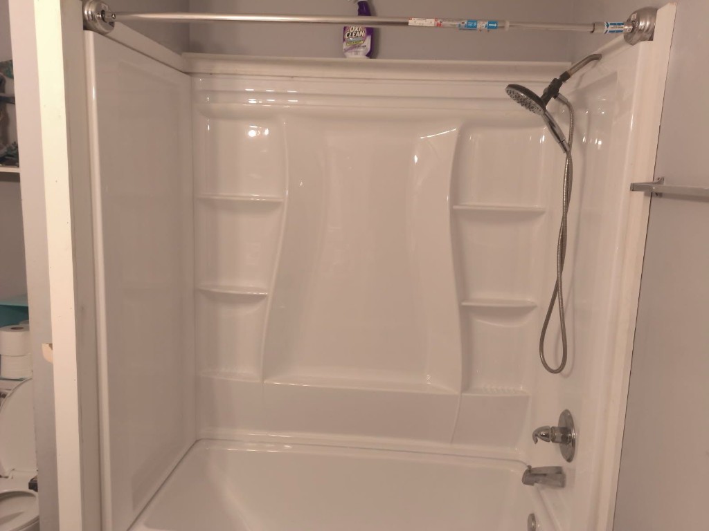 Wide angle view of completed white tub and shower surround installation showing full enclosure with chrome fixtures and corner shelves