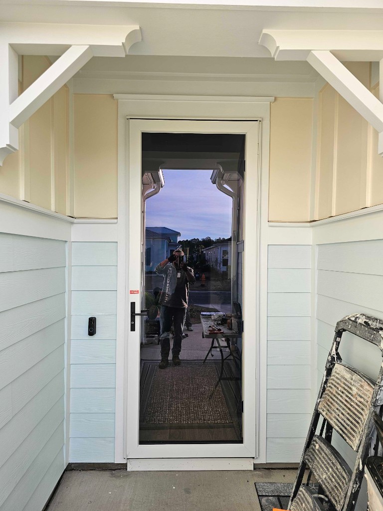 Full-view white storm door with black hardware on a home with coastal siding
