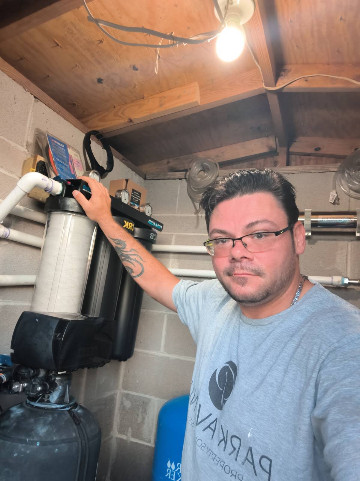 Park Avenue technician beside a completed whole-house water filter installation with three filter canisters, pressure gauges, media tank, pressure tank, and UV sterilizer in a Florida utility room